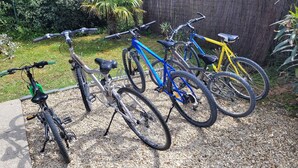 A row of bicycles parked on a gravel surface, with a fence and greenery in the background.