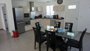 A modern kitchen with stainless steel appliances, a glass dining table, and black chairs.