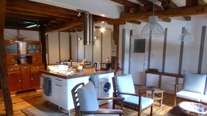 Una cocina acogedora con armarios de madera, una isla central y una lavadora. Hay dos sillas de madera y una mesa con un bol encima.