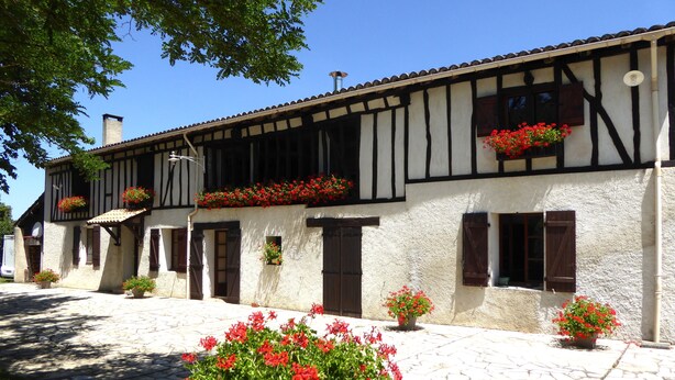 Un edificio tradicional con entramado de madera, macetas con flores en las ventanas superiores y un patio empedrado.