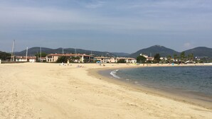 A wide sandy beach with a calm sea, buildings in the background, and mountains in the distance. - Apartment in lake city of Grimaud harbor with beautiful view (Port Grimaud)