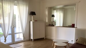 Een kamer met een houten vloer, een witte bank, een kleine tafel, een kast en een raam met dunne gordijnen.