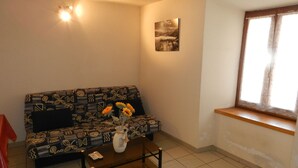 Una sala de estar con un sofá estampado, una mesa de centro con un florero, un cuadro en la pared y una ventana con cortinas.