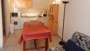 Una cocina compacta con armarios de madera, lavadora, microondas y una mesa de comedor con sillas.
