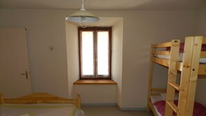 Una habitación pequeña y bien iluminada con una cama litera, una cama individual, una ventana con cortinas y una lámpara en el techo.