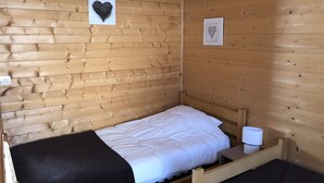 A single bed with a white mattress and black blanket, a bedside table with a lamp, and two heart-shaped decorations on the wooden walls. - Independent wooden chalet  (Le Tholy)