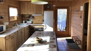 A wooden cabin kitchen with a central island, a refrigerator, and a window overlooking a deck. - Independent wooden chalet  (Le Tholy)