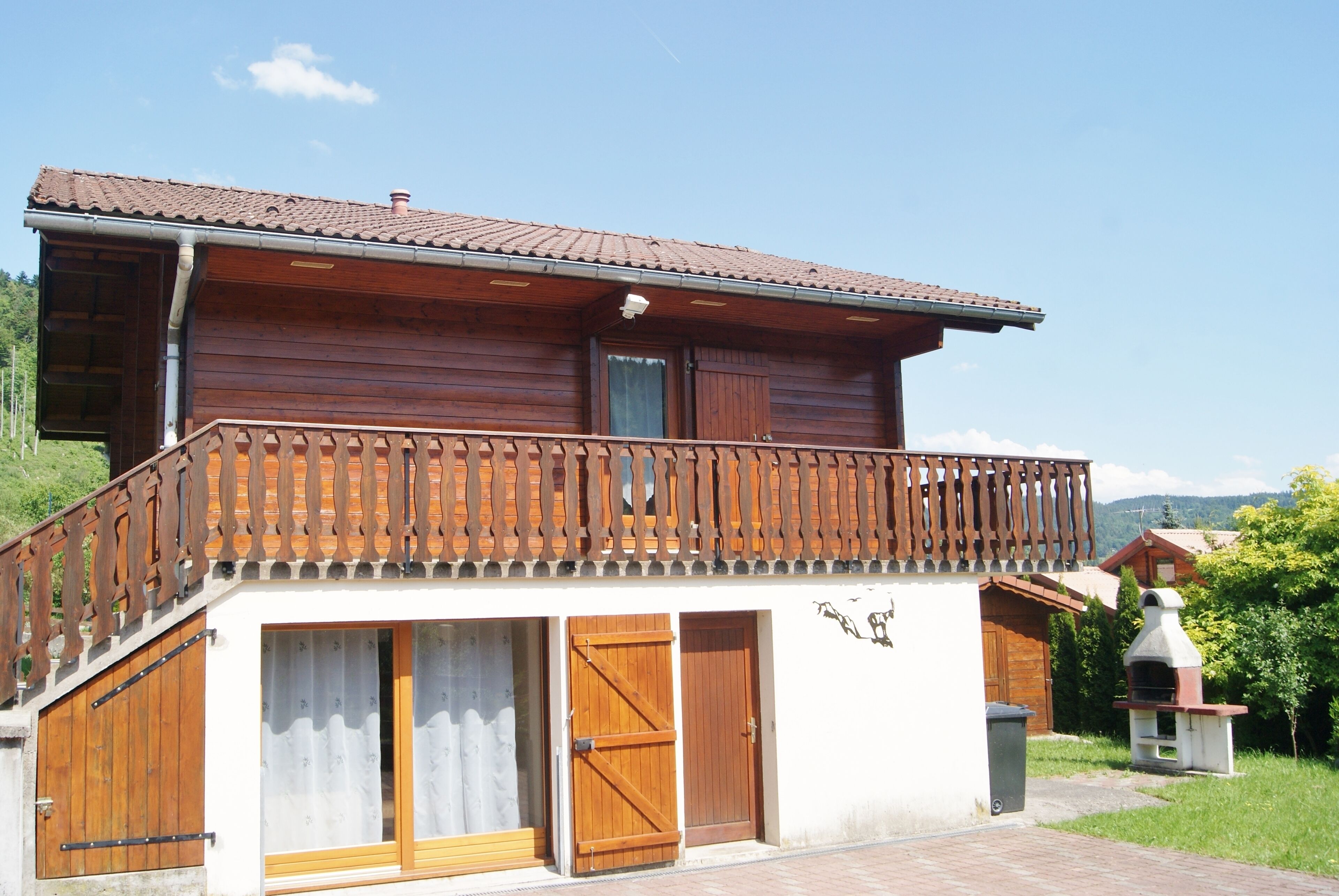 A two-story wooden house with a balcony, a chimney, and a small outdoor grill.