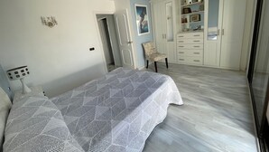 Un dormitorio con cama, una silla, un armario y una puerta que da a otra habitación.