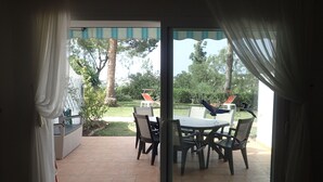 Un patio con mesa y sillas, un pequeño jardín y vistas a árboles y un césped.