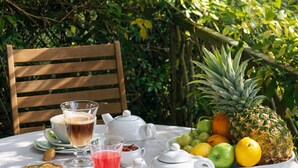 A table set outdoors with a white tablecloth, a wooden chair, a teapot, cups, a glass of red drink, a bowl of fruit, and toast. - Romantic cottage with private heated pool - 2 pers - Bassin d'Arcachon (Lanton)