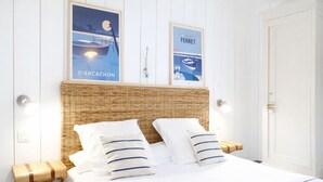 A bed with white bedding and striped pillows, a wicker headboard, and two posters on the wall. - Romantic cottage with private heated pool - 2 pers - Bassin d'Arcachon (Lanton)