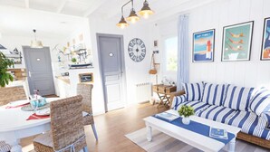 A bright, nautical-themed living room with a striped sofa, wicker chairs, and a dining table set for four. - Romantic cottage with private heated pool - 2 pers - Bassin d'Arcachon (Lanton)