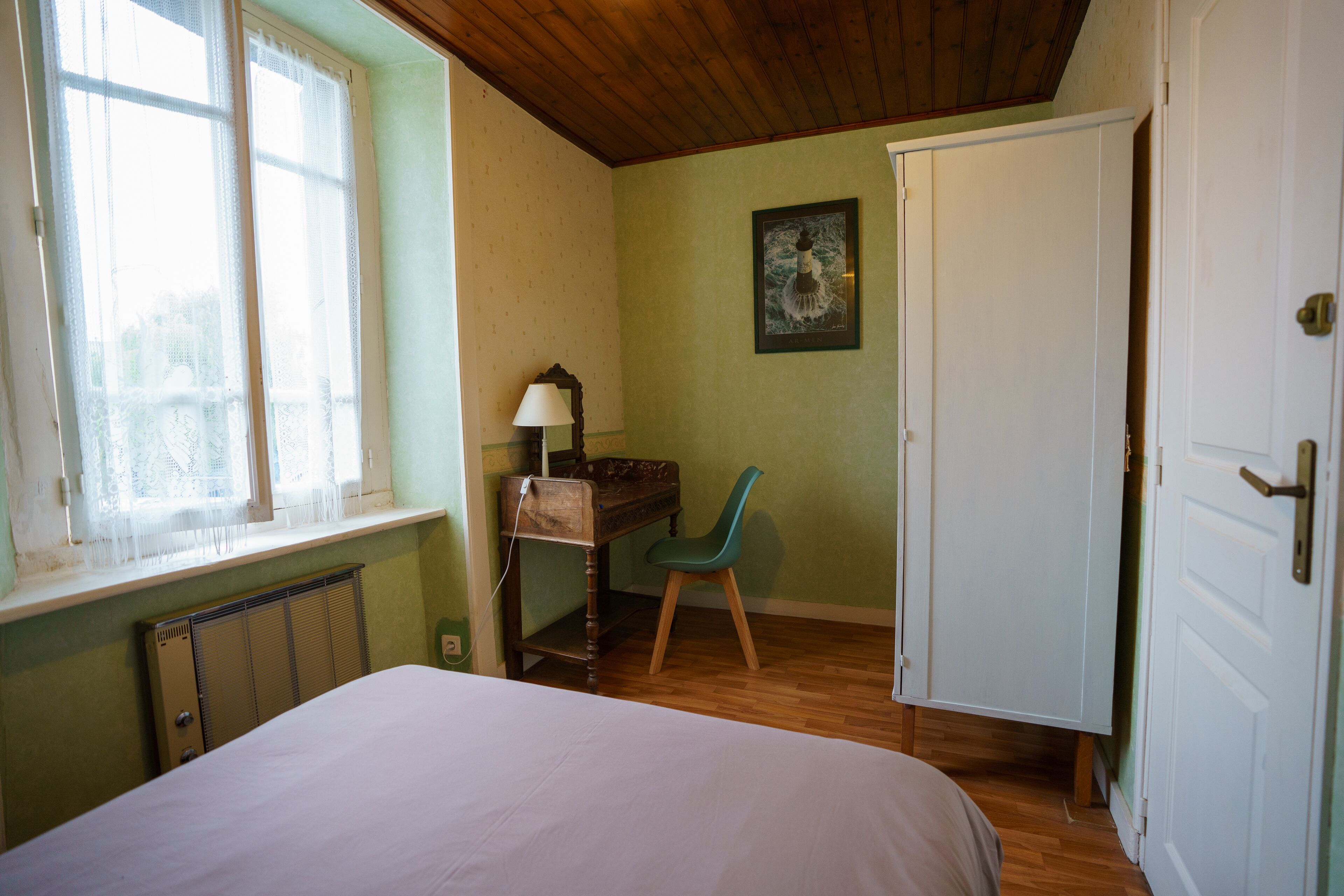 Ein Schlafzimmer mit Bett, Schreibtisch, Stuhl, Heizkörper, Fenster und Tür.