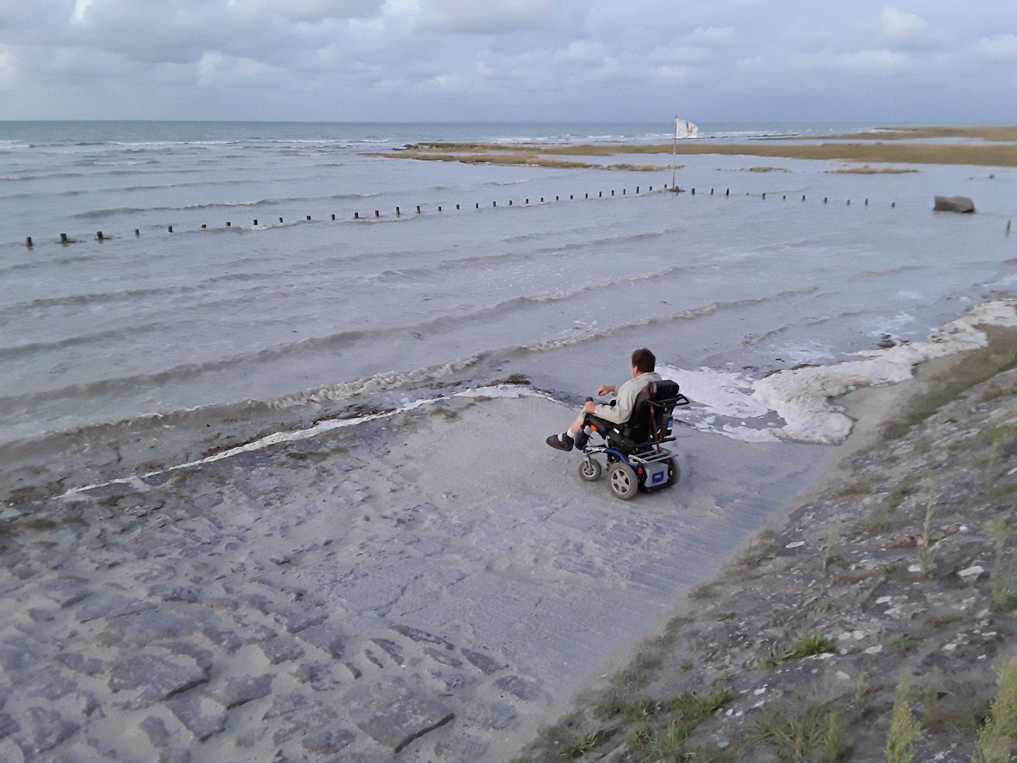 En rullstol på en sandstrand med havet i bakgrunden.