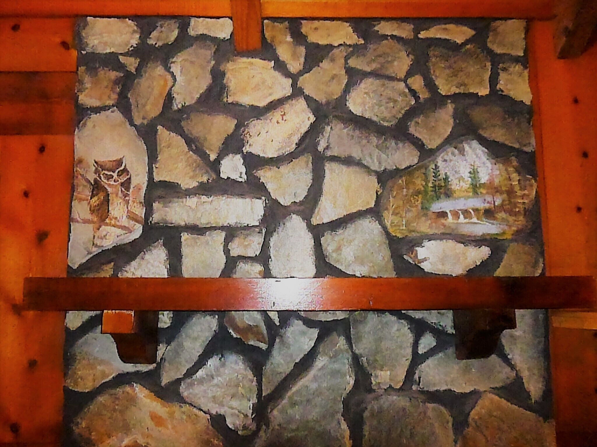 A stone wall with a painting of an owl and a landscape.