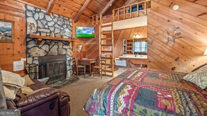 Interior acogedor de una cabaña con chimenea de piedra, paredes de madera, una litera, un escritorio y un televisor.