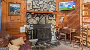 Interior acogedor de una cabaña con chimenea de piedra, paredes de madera, televisor montado y zona de comedor.