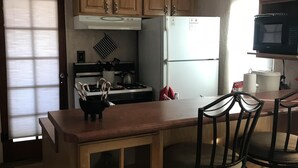 A kitchen with wooden cabinets, a white refrigerator, a stove, and a microwave. There is a wooden island with chairs and a glass-fronted cabinet. - LAVENDER  LIZARD B Upper Unit CASITAS (Farmington)