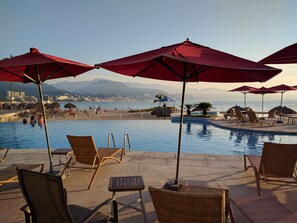 Un espace aménagé au bord de la piscine, avec des chaises longues et des parasols, offrant une vue sur la plage et les montagnes.