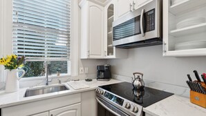 Une cuisine moderne avec des meubles blancs, un four à micro-ondes encastré, un four et une bouilloire sur la cuisinière.