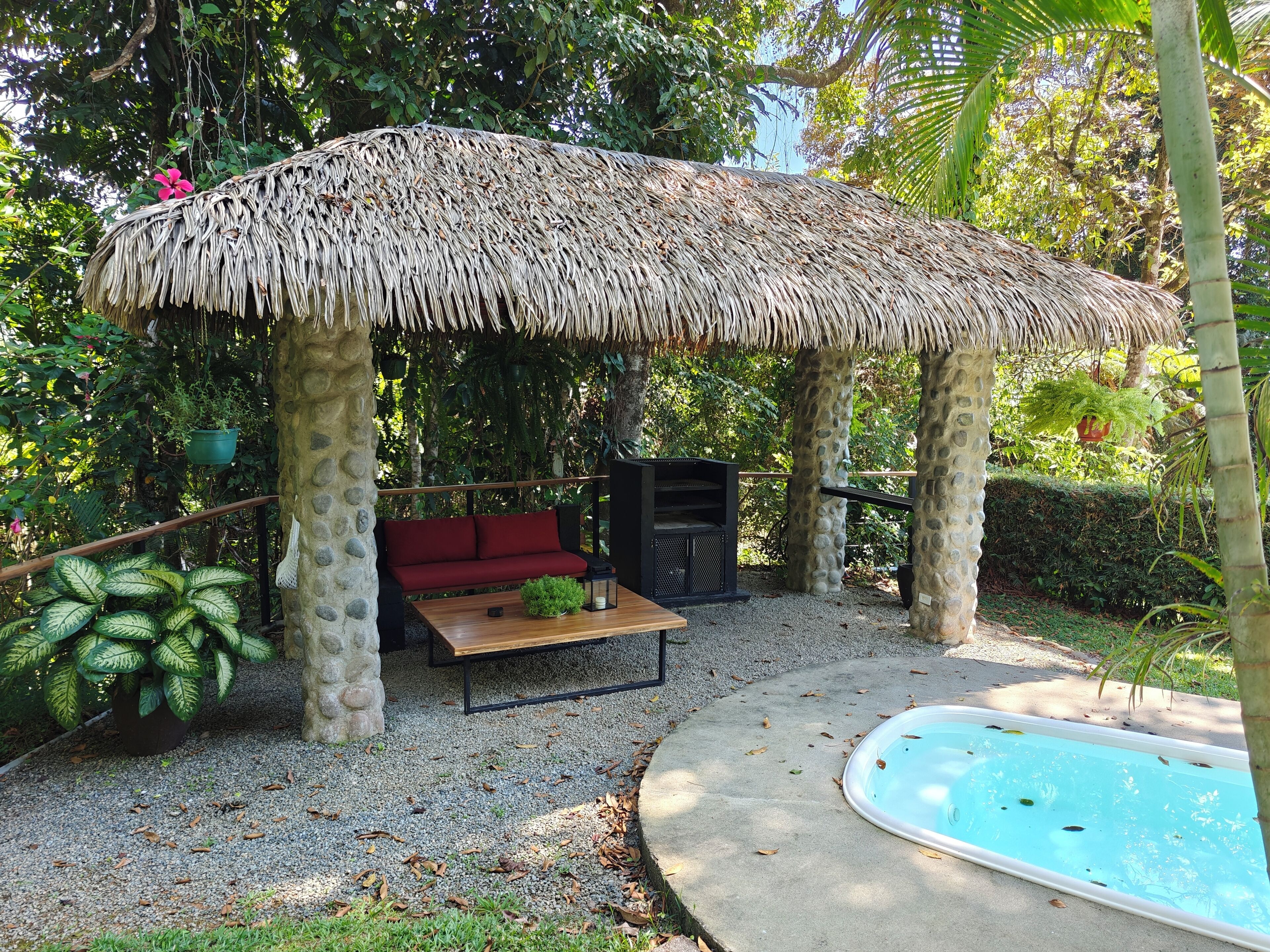 A thatched gazebo with a bench, surrounded by greenery and a small pool.