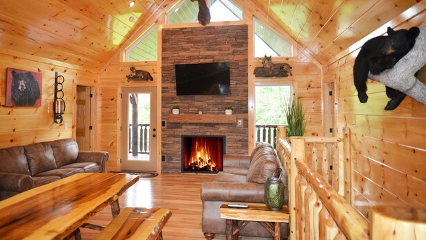 A cozy cabin interior with a stone fireplace, leather furniture, and a bear mounted on the wall. - Luxury 4 King Suites, 4 Bath Log Cabin Close to Town & Trolley (Gatlinburg)