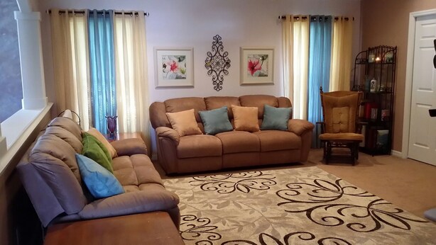 Ein Wohnzimmer mit braunen Sofas, einem gemusterten Teppich und zwei gerahmten Blumenbildern an der Wand.