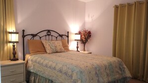 Ein Schlafzimmer mit einem Bett, einem Nachttisch, einer Lampe, einem Deckenventilator und Vorhängen.
