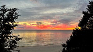 Ein Strand mit Sonnenuntergang, ruhigem Wasser und Bäumen, die das Bild einrahmen.