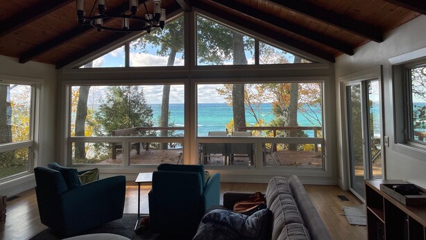 Ein geräumiges Zimmer mit großem Fenster zum Strand und Meer, Holzbalkendecke und einer gemütlichen Sitzecke mit Sofa und Sesseln.