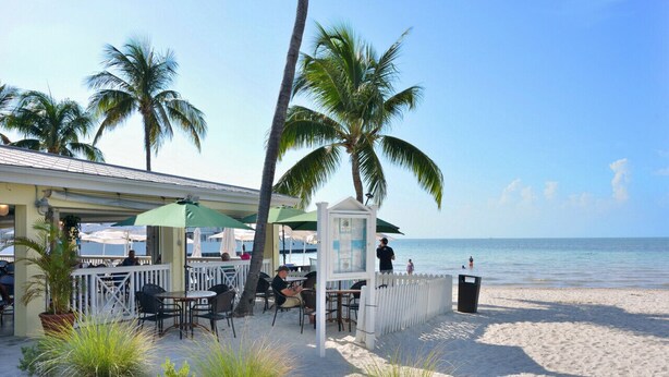 Ein Restaurant am Strand mit Außenbestuhlung, Palmen und Meerblick.
