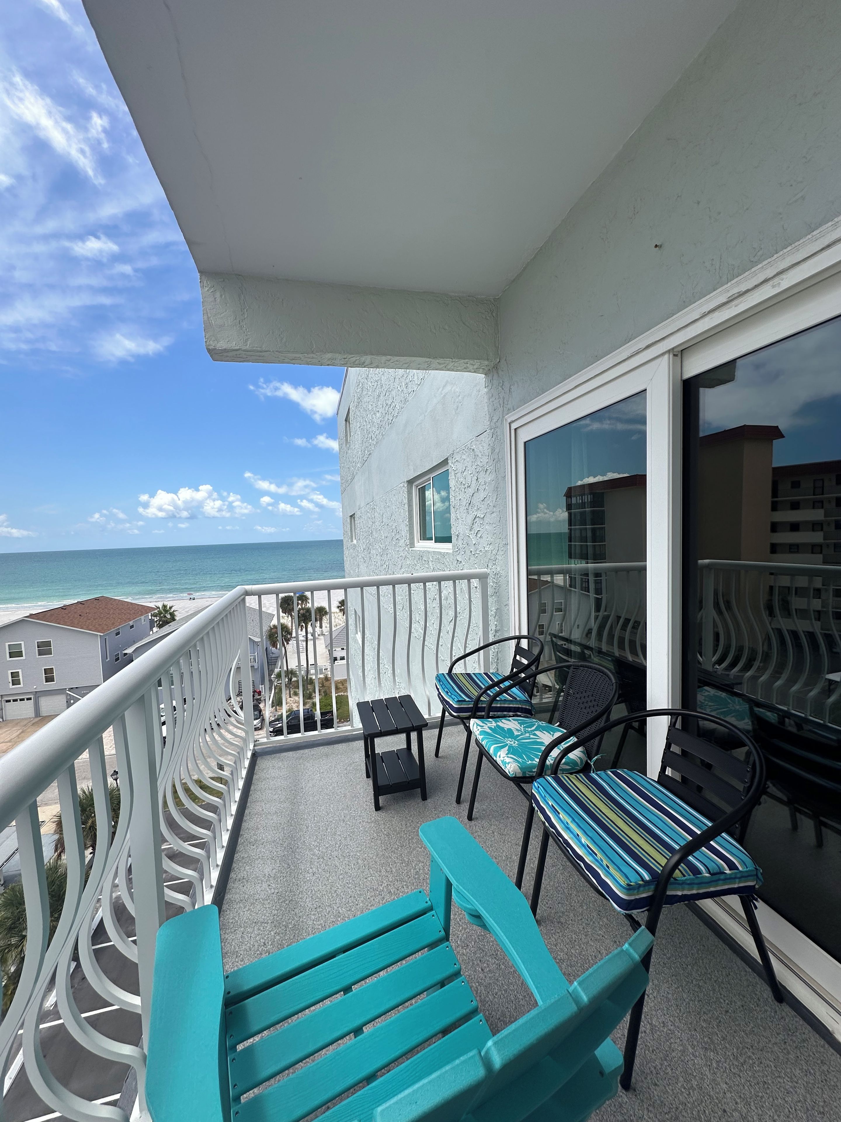 A balcony with a view of the ocean, a table, two chairs, and a bench.