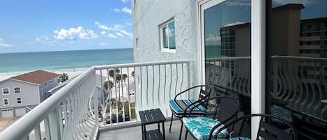 A balcony with a view of the ocean, a table, two chairs, and a bench.