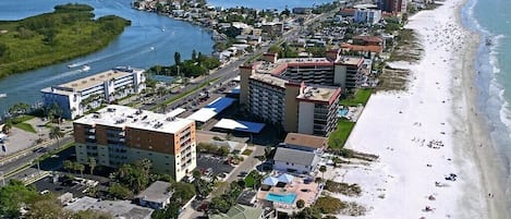 Una vista aerea di una città costiera con una spiaggia, un porto turistico e diversi edifici, tra cui hotel e zone residenziali.