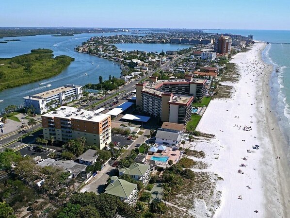 Eine Vogelperspektive einer Küstenstadt mit Strand, einer Marina und mehreren Gebäuden, darunter Hotels und Wohngebiete.