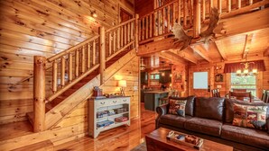 L’intérieur d’une cabane en rondins, avec un escalier en bois, un salon doté d’un canapé en cuir et un coin cuisine.