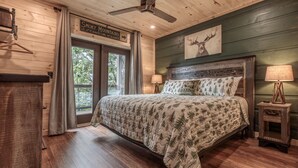 Une chambre à coucher comprenant un lit, une table de chevet, une lampe, un ventilateur de plafond et un panneau indiquant que l’on se trouve dans la région des Smoky Mountains.