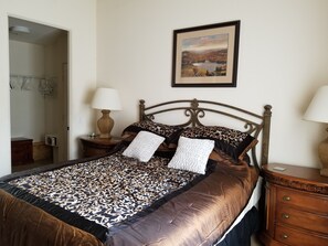 Un letto rifatto con lenzuola a fantasia, un comodino con una lampada e un quadro appeso alla parete.