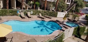 Una piscina con lettini da relax e una piccola zona prendisole, circondata da un recinto bianco e palme.