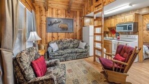 Un interior de cabaña acogedor, con detalles de madera, un sofá, un sillón mecedor y una zona de cocina.