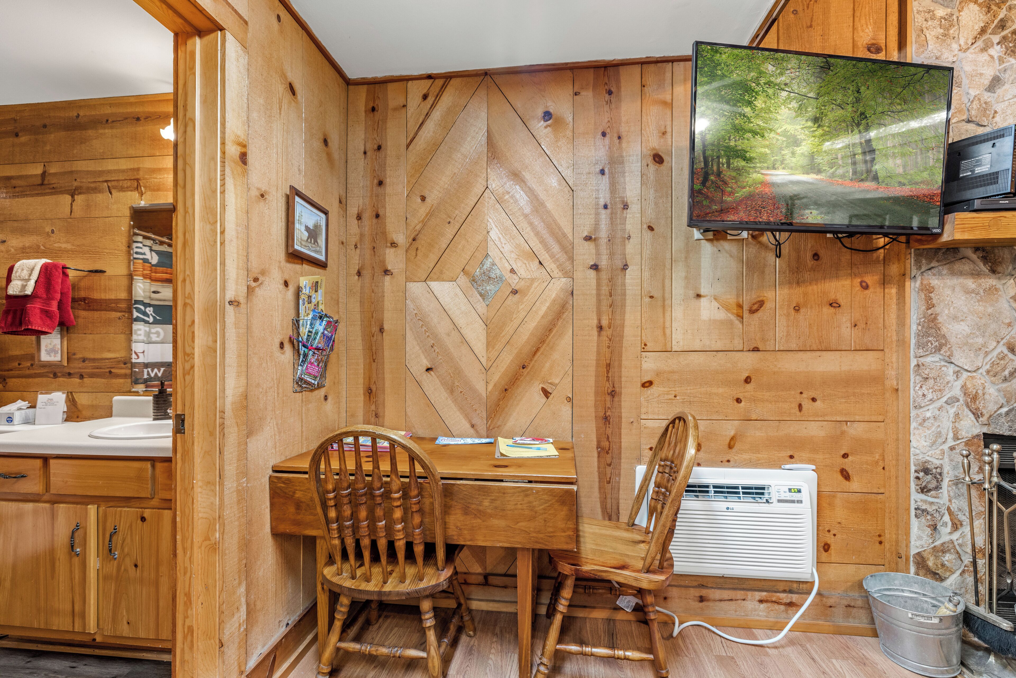 A wooden interior with a dining table, chairs, a television, and a stone wall.