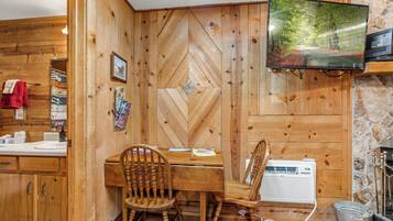 A wooden interior with a dining table, chairs, a television, and a stone wall.