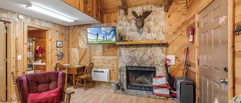 A wooden cabin interior with a fireplace, a television, and a dining area.