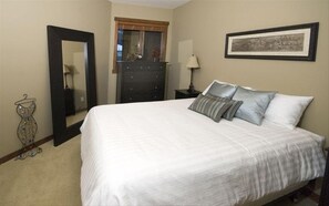 Cozy retreat with a large bed, dresser, mirror, and artwork.