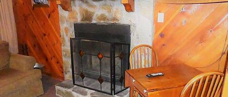 A cozy room with a stone fireplace, wooden walls, a television mounted above the fireplace, and a small table with chairs.