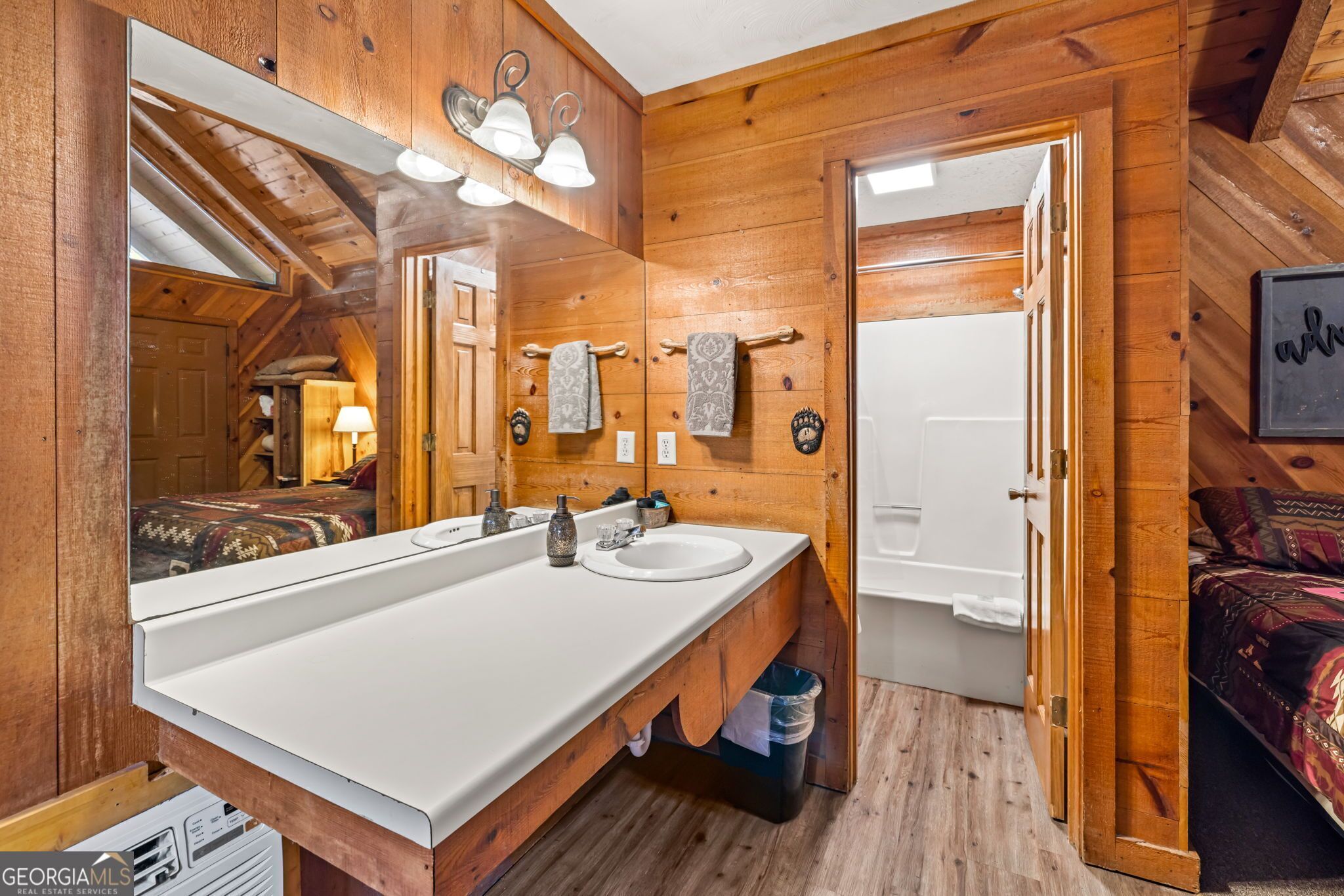 A wooden cabin bathroom with a large mirror, two sinks, and a shower.
