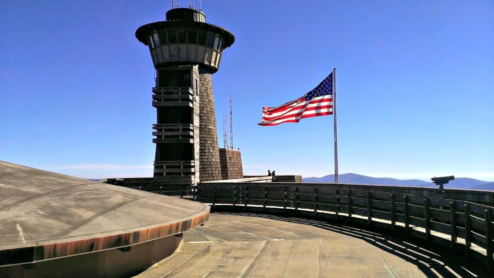 A control tower with an American flag, a clear sky, and mountains in the background.