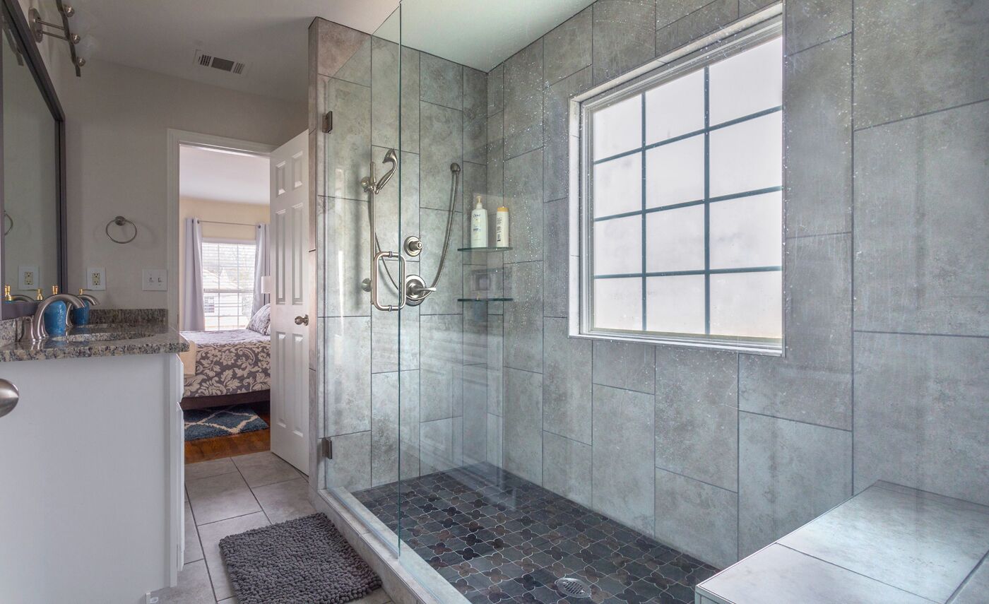 A modern bathroom with a glass-enclosed shower, a large window, and a vanity with a mirror and sink.