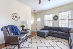 A living room with a leather chair, a gray sectional sofa, a small table with a lamp, and a wall clock. - Close to Downtown, Midtown, GT, GWCC and Mercedes-Benz Stadium (Atlanta)
